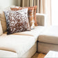 Hair-on leather cushion placed on a neutral-toned sofa with throw blankets, adding boho-chic elegance and warmth to a cozy living room setup.

