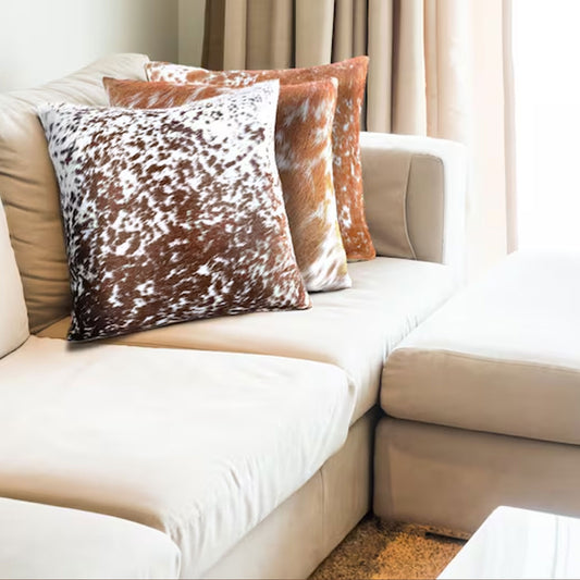 Hair-on leather cushion placed on a neutral-toned sofa with throw blankets, adding boho-chic elegance and warmth to a cozy living room setup.

